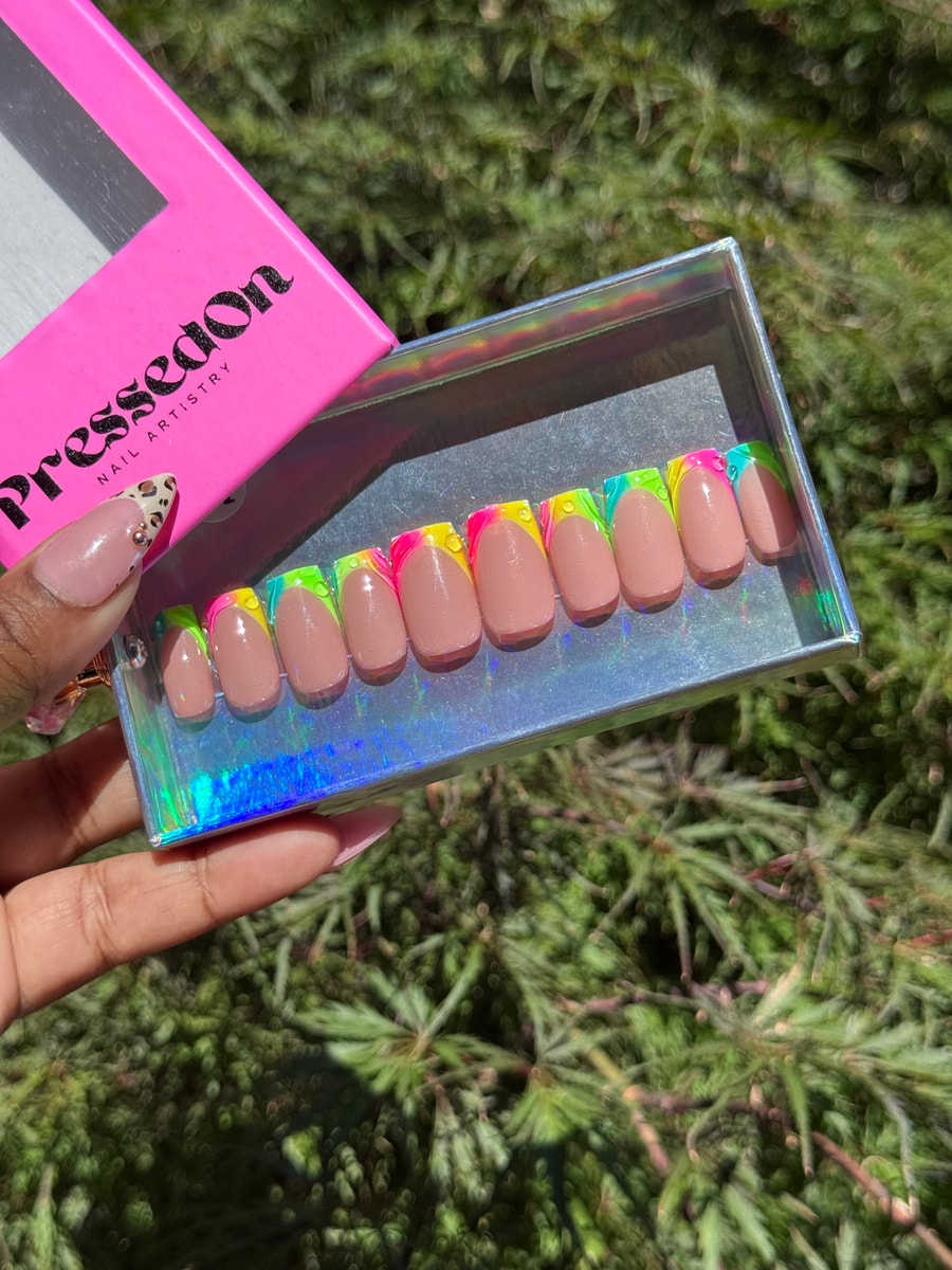 These are super short press-on nails with a nude base color. The nails have brightly colored neon French tips with green, yellow, pink, and blue shades.