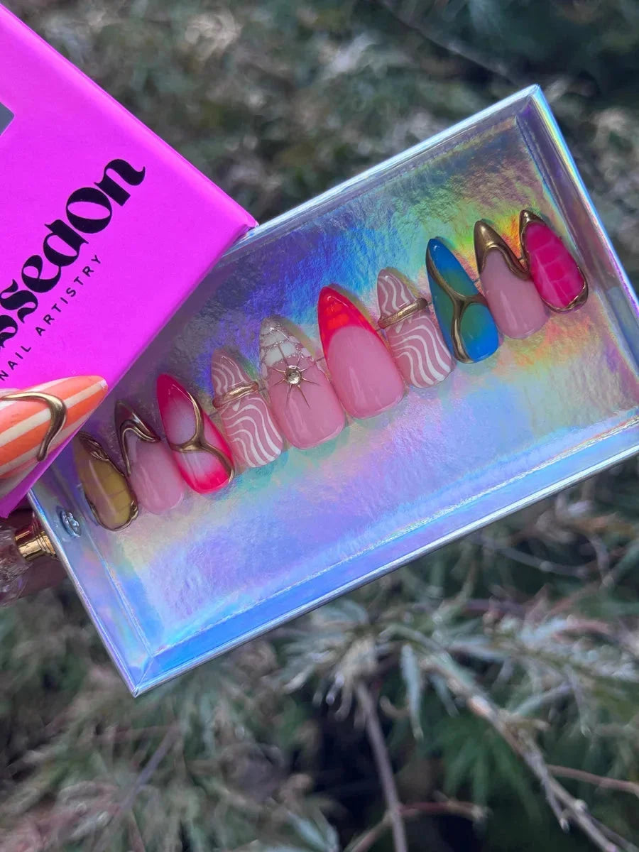 Short almond press-on nails featuring abstract art designs in neon colors with white patterns, gold accents, and subtle sparkle.