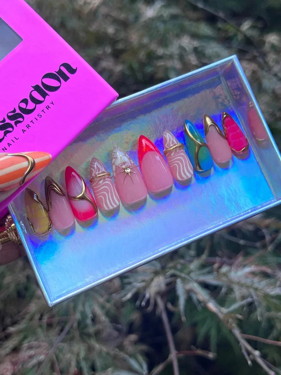 Short almond press-on nails with abstract designs, neon colors, gold accents, and varied French tips in red, pink, gold, and blue.