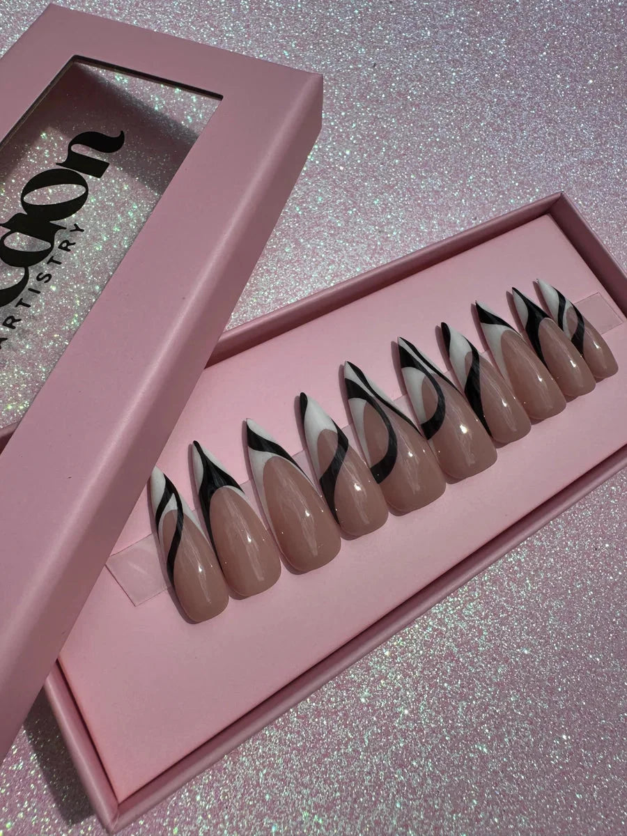 These are nude almond press-on nails with a black and white abstract swirl design. The design is on the tips of the nails.