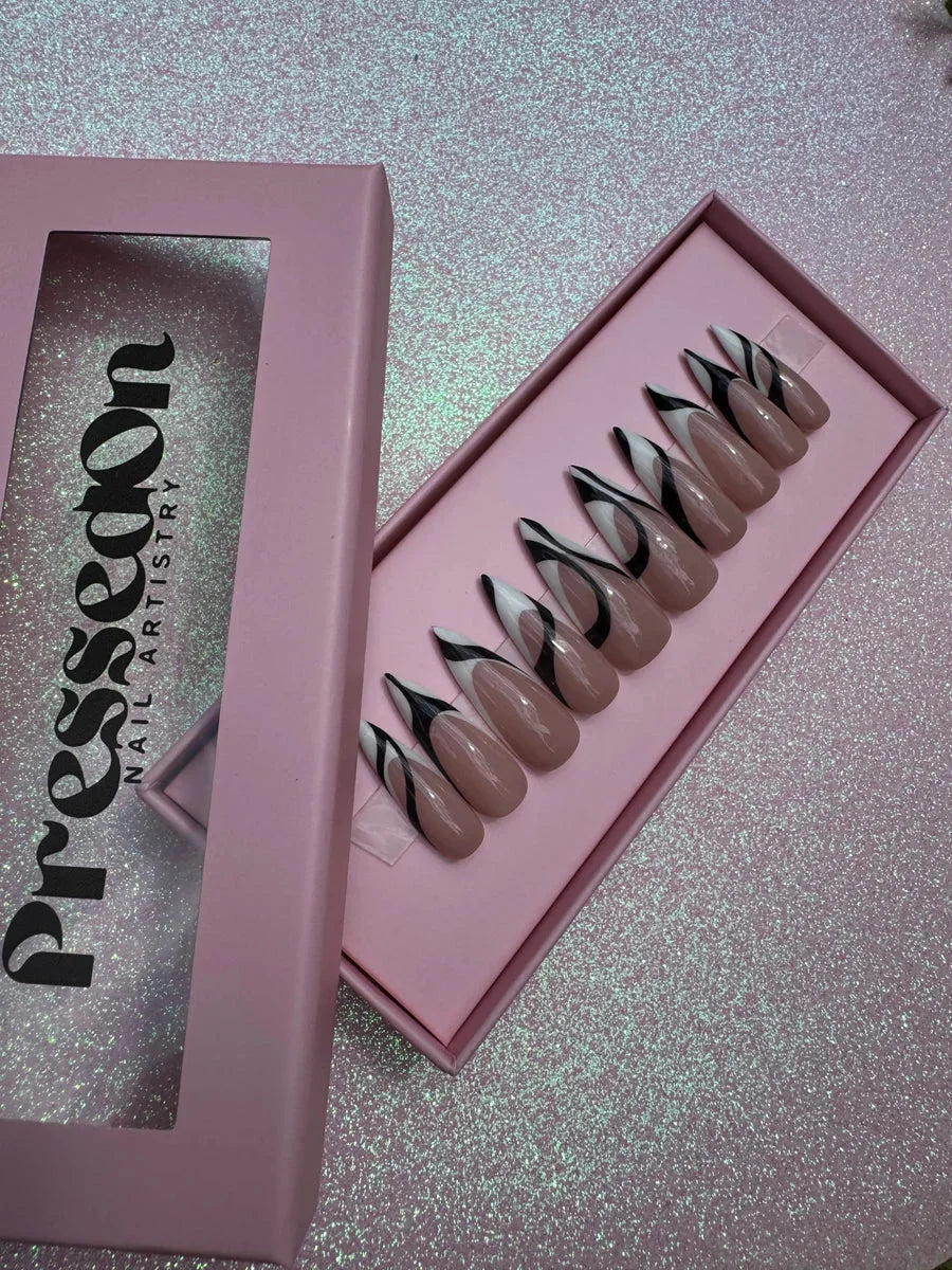 Nude almond-shaped press-on nails with a black and white abstract swirl design on each nail.