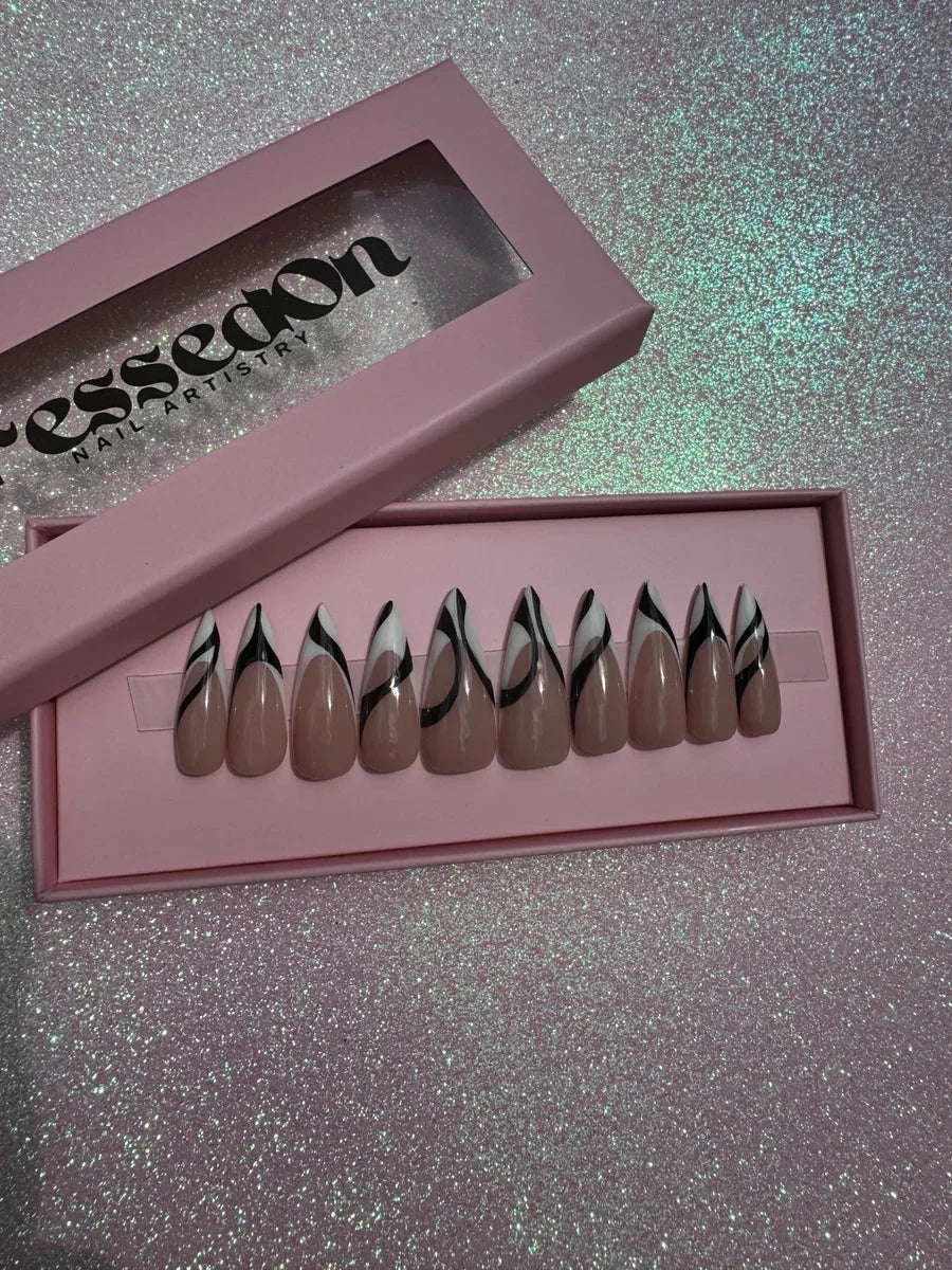 Almond-shaped nude press-on nails with a black and white abstract swirl design. The design accents each nail.