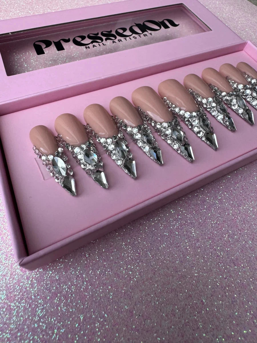 Nude stiletto press-on nails adorned with silver rhinestones and sparkling crystals at the base. The long length and stiletto shape offer a bold and glamorous look.