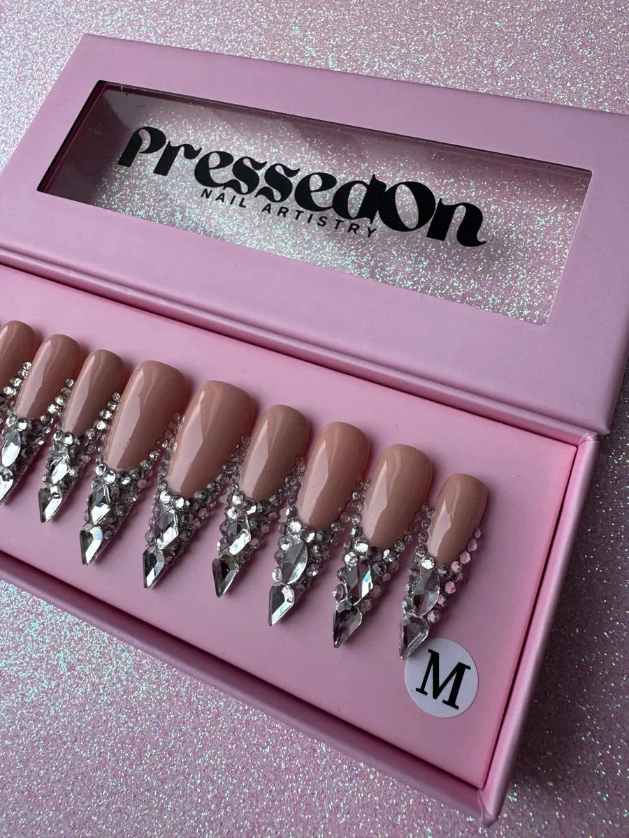 Nude long stiletto press-on nails with a cascading design of sparkling rhinestones and clear crystals at the base.