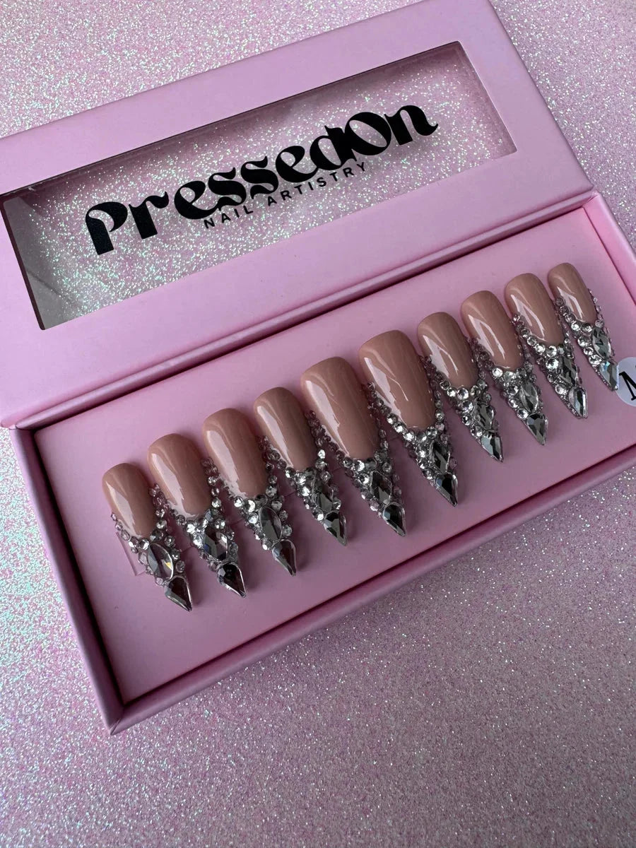 Nude stiletto press-on nails featuring cascading rows of silver rhinestones and pointed diamond accents for a glamorous bling look.