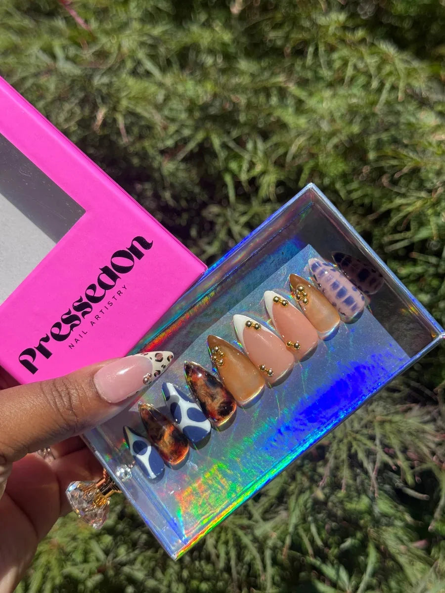 Press-on nails with a mix of blue cheetah print and nude designs, some adorned with gold embellishments.