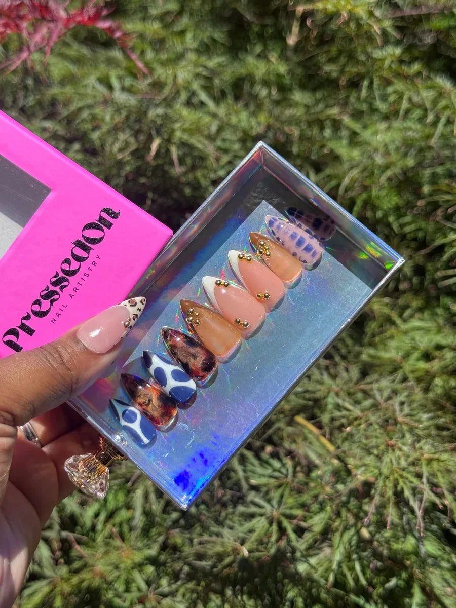 Set of short press-on nails displaying various designs, including cheetah print in blue, tortoise shell, nude with white tips, nude with gold accents, and blue marbled nail patterns.
