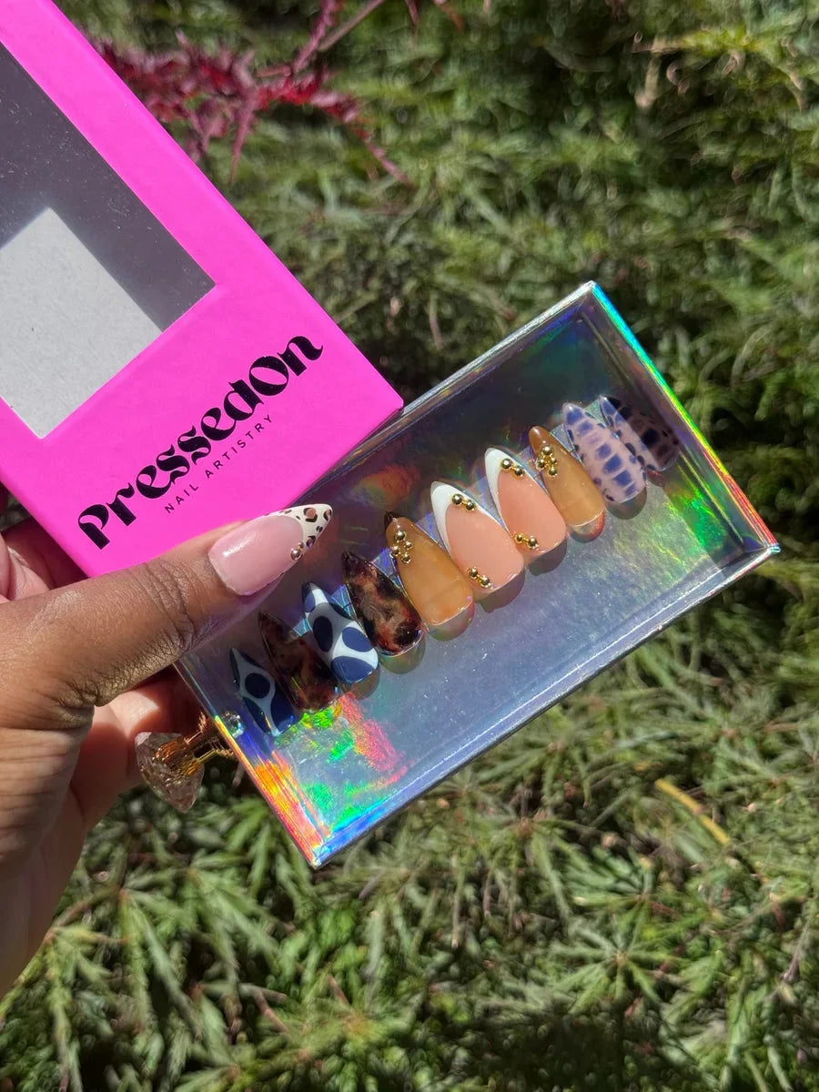 Short press-on nails with a nude cheetah design, alongside blue cow print, nude, tortoise shell, and animal print accent nails.