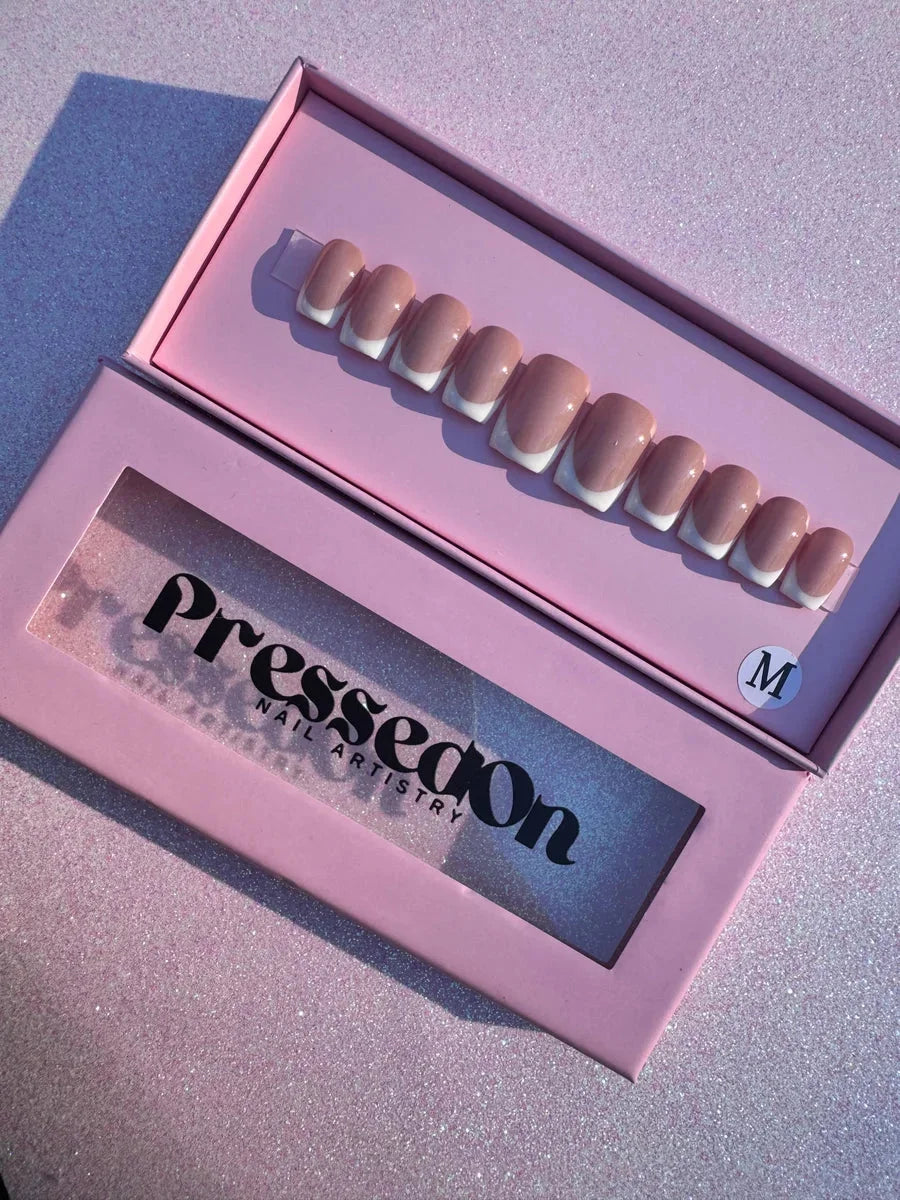 Short, square press-on nails featuring a French manicure design with white tips. The nails have a nude base.