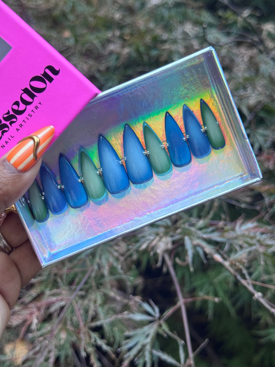 Blue and green stiletto press-on nails with a blended Ocean Aura design. Each nail is accented with a tiny silver rhinestone.