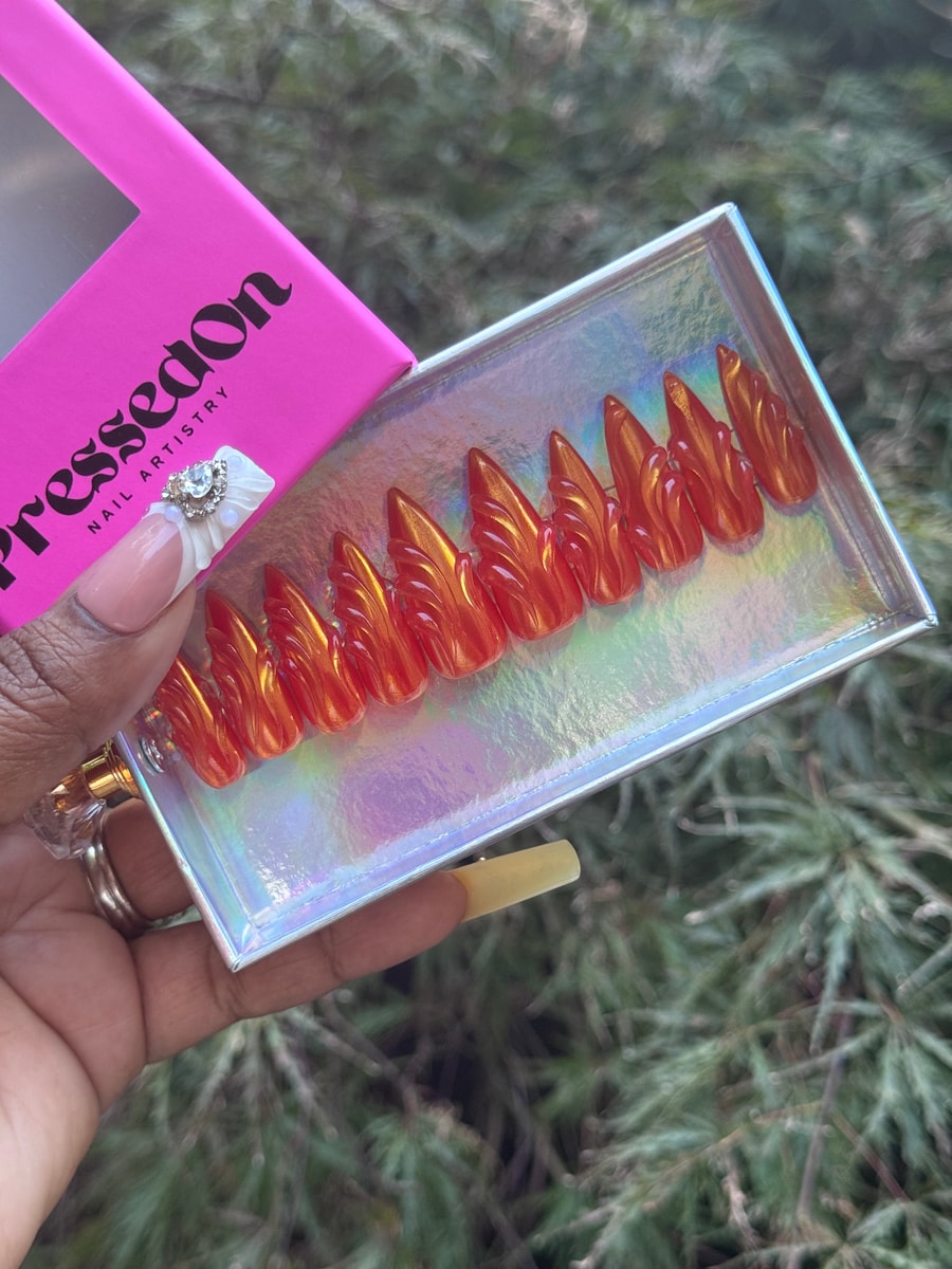 Set of medium-length orange stiletto press-on nails with a glossy finish and a sculpted wing design. 