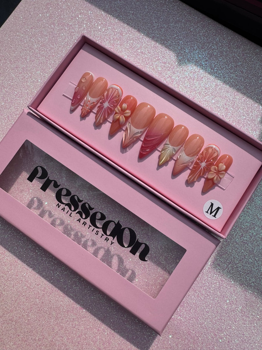 Medium-length press-on nails with orange slice and floral designs on a neutral base.