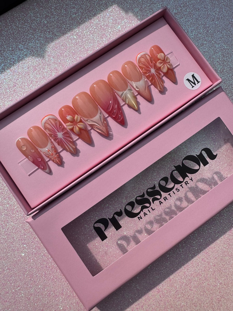 Medium press-on nails featuring a fresh orange slice design and delicate floral accents. The nails are mostly orange and white, with clear resin details.