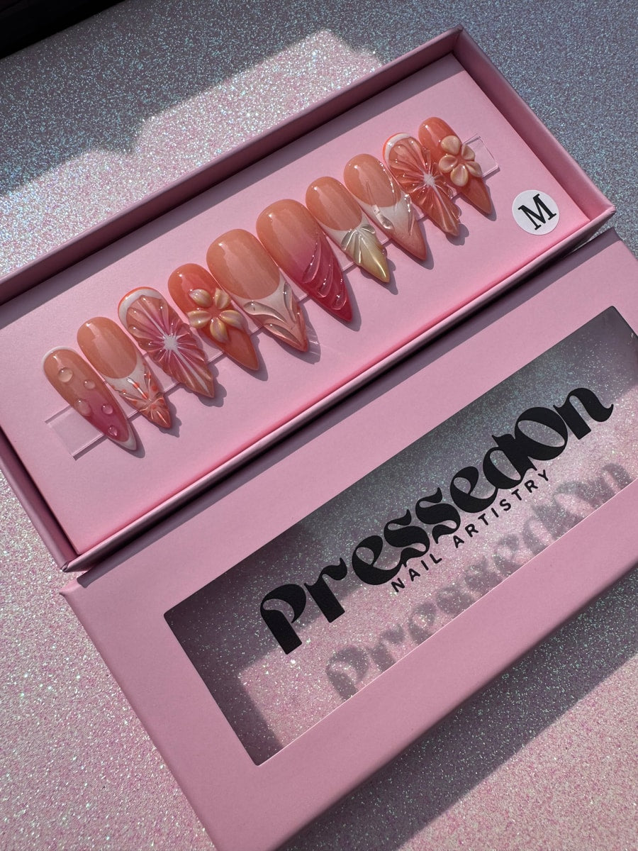 Medium-length press-on nails with an orange slice design and white accents, including 3D flower embellishments.