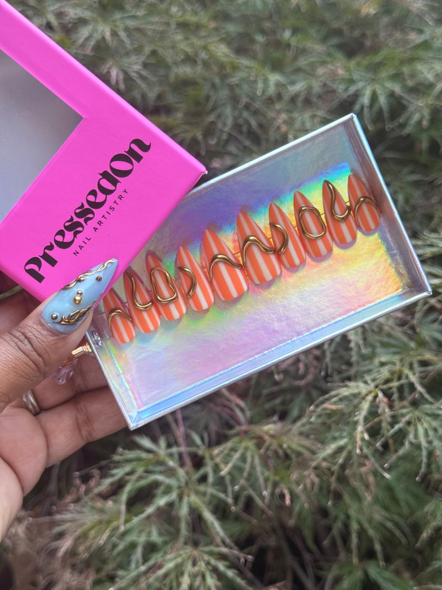 Set of orange and white striped stiletto press-on nails, each adorned with a unique gold wire accent.