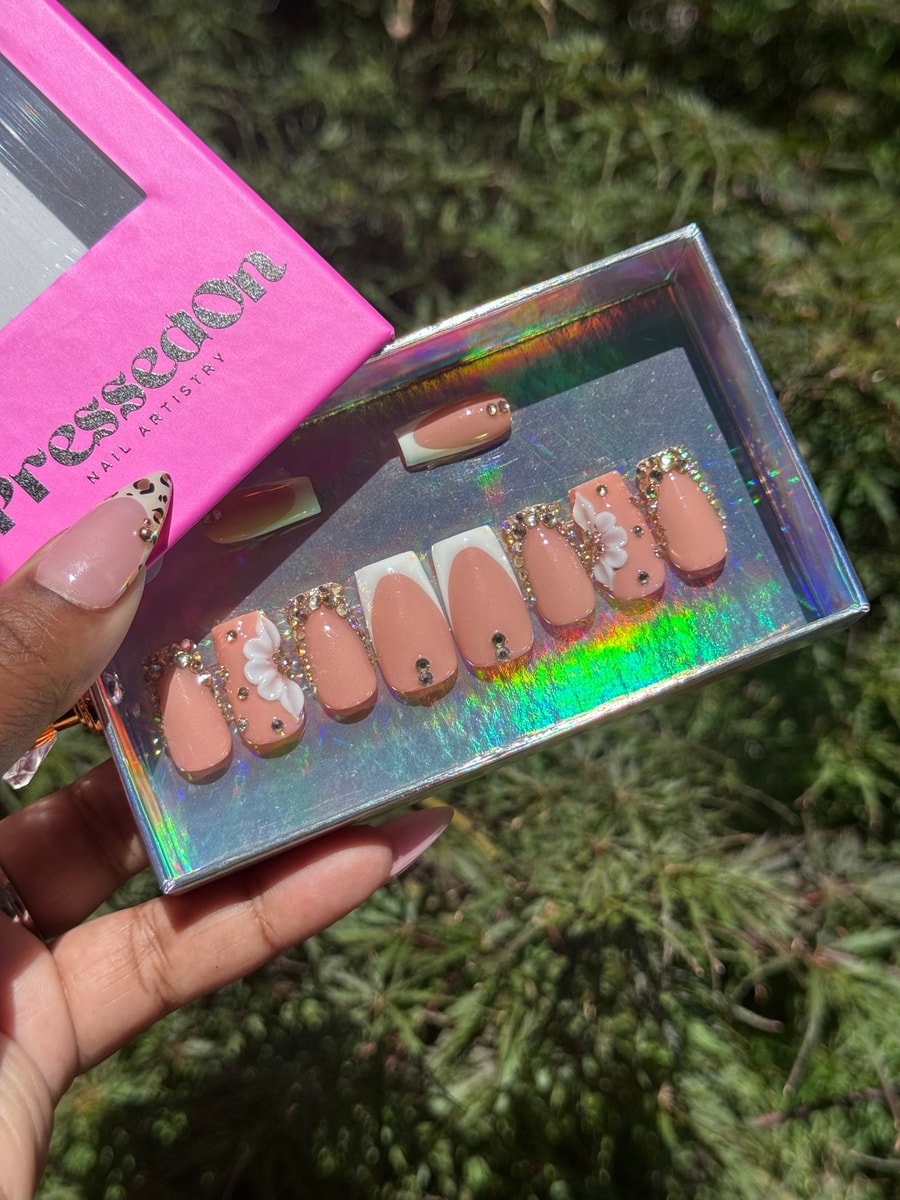 Set of super short peach press-on nails with white French tips and rhinestone accents. Some nails have 3D flower decorations.