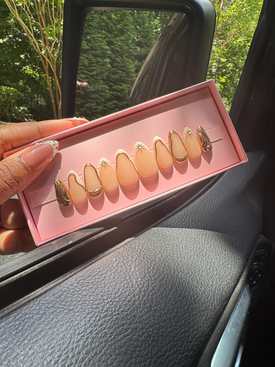 Peach super short press-on nails are detailed with gold trim and rhinestone accents. Two nails feature a solid gold design.