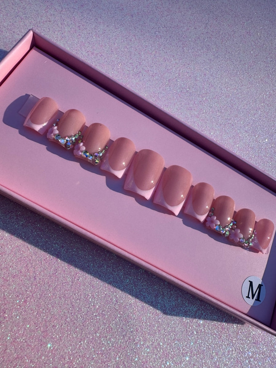 Pink, super short, French tip press-on nails with bling. Some nails have floral and rhinestone decorations.