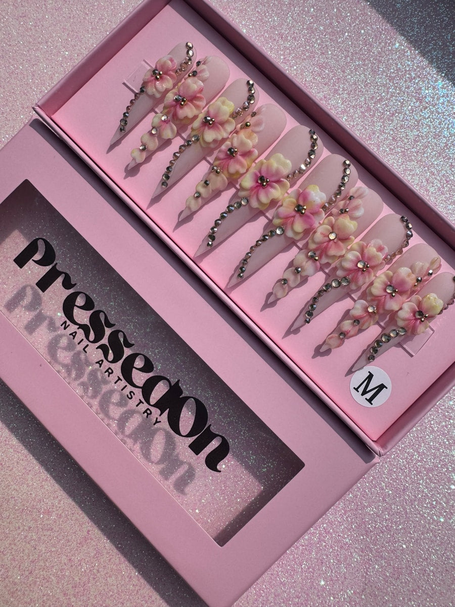 Light pink extra long stiletto press-on nails decorated with 3D pink and yellow flowers and silver rhinestones along the sides.