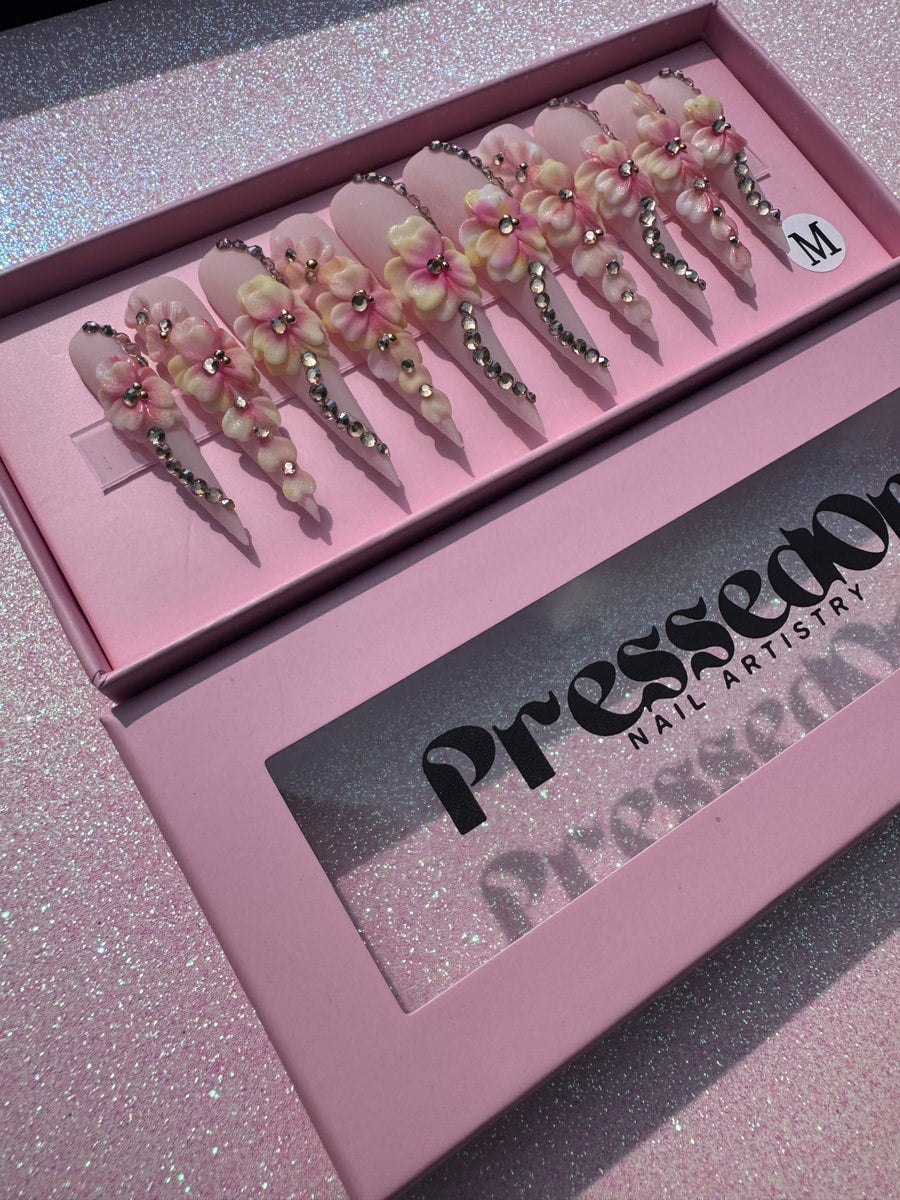 Pink stiletto press-on nails with 3D flower designs and rhinestone detailing.