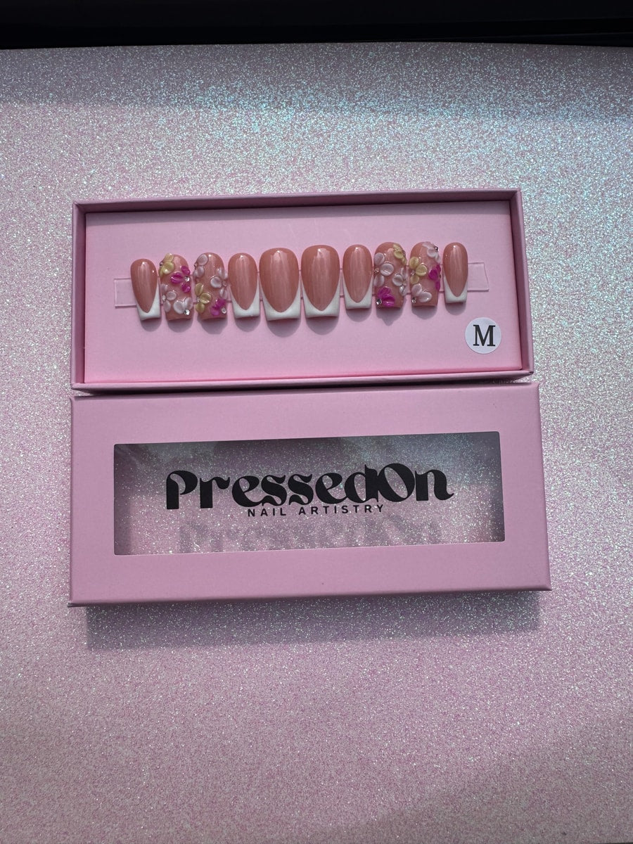 Short pink press-on nails with white French tips and 3D flower decorations in shades of white, pink, and yellow.