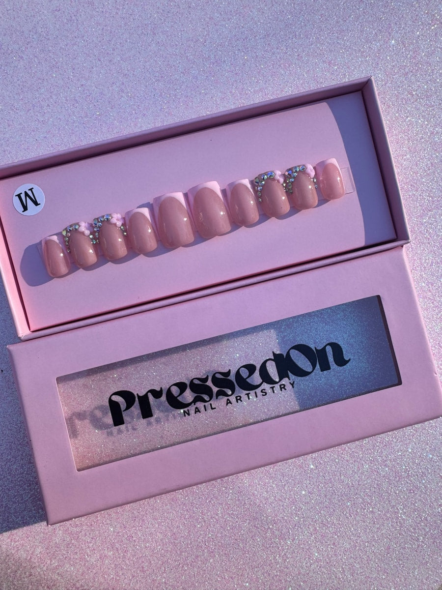 Set of pink super short press-on nails featuring a white French tip and small rhinestone and flower accents on some nails.