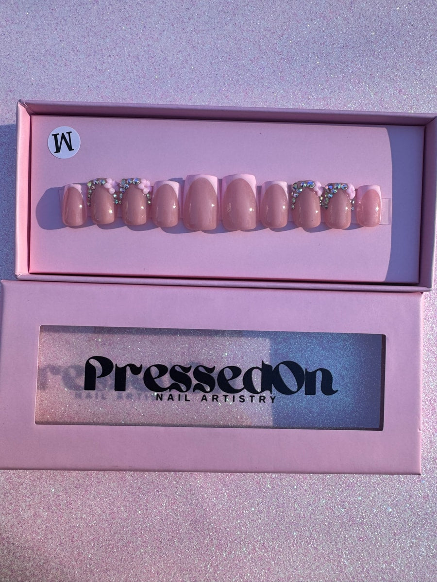Super short pink press-on nails with French tips are decorated with rhinestones and flower charms.