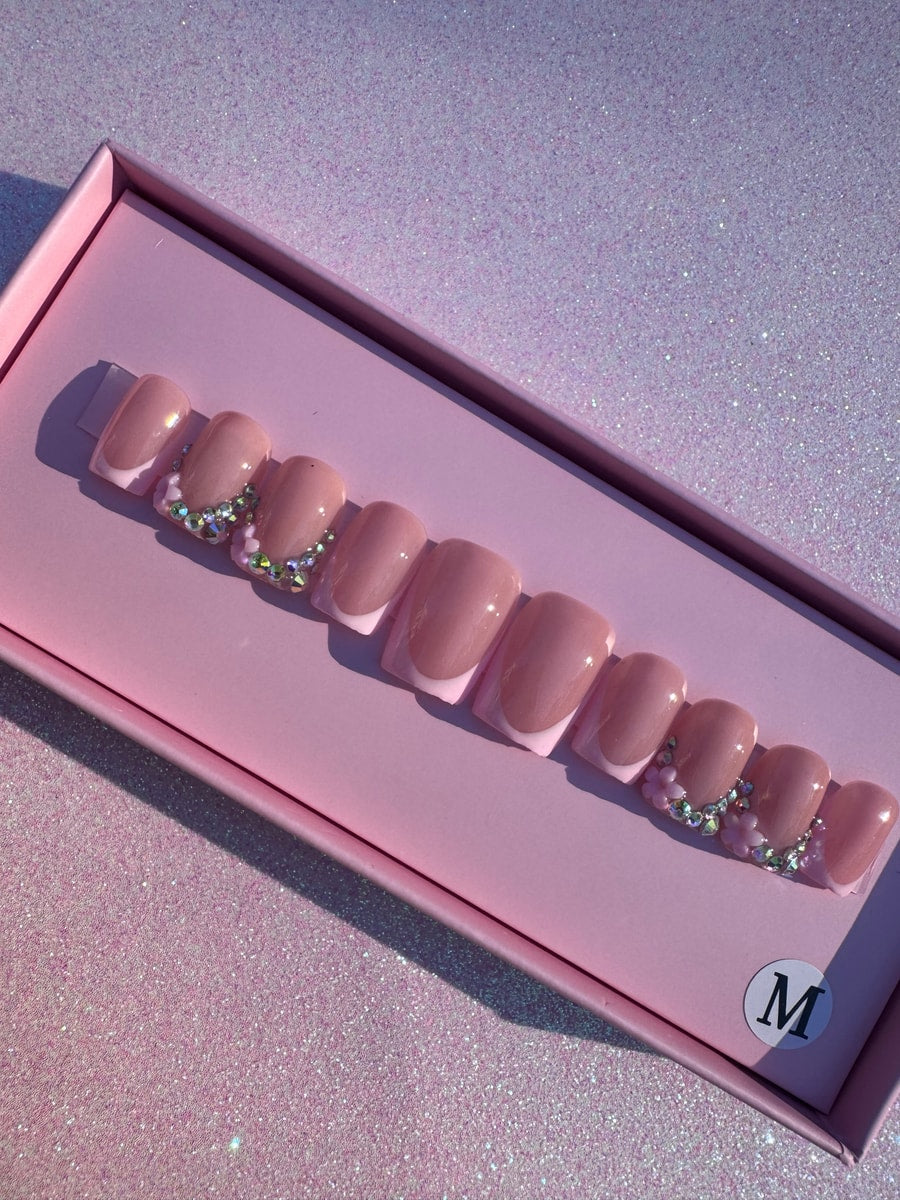 Set of short pink press-on nails with a French manicure design and rhinestone accents near the cuticle.