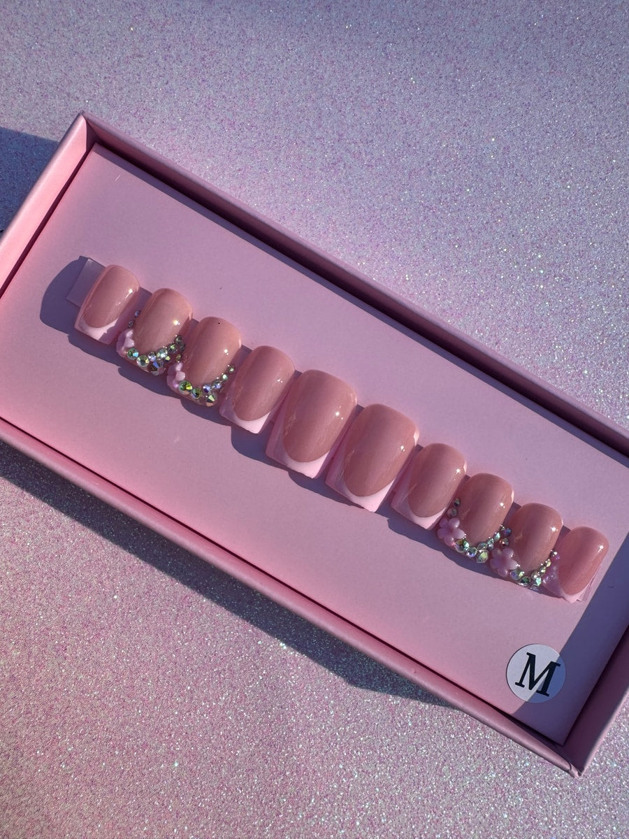 Set of short pink press-on nails with a white French tip. Three nails on each end are decorated with rhinestones and tiny flowers.