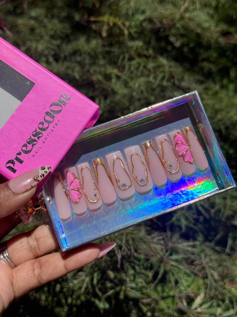 Pink press-on nails with gold accents and rhinestone details. Two nails are decorated with 3D pink hibiscus flower charms.