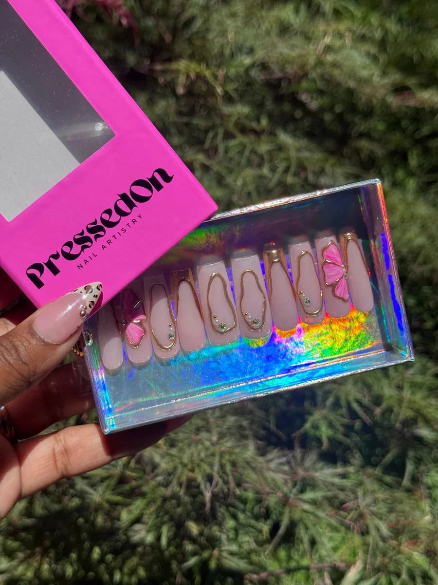 Pink press-on nails featuring gold outlines, small gem accents, and a pink hibiscus flower. 