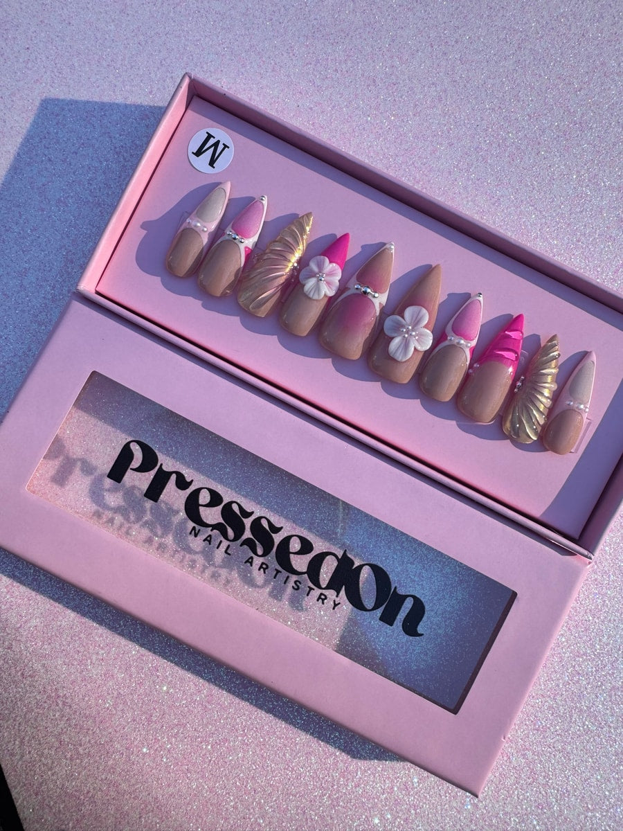 Set of medium-length pink press-on nails with pearl details, gold seashell accent nail, 3D white flower charms, and bright pink tips.
