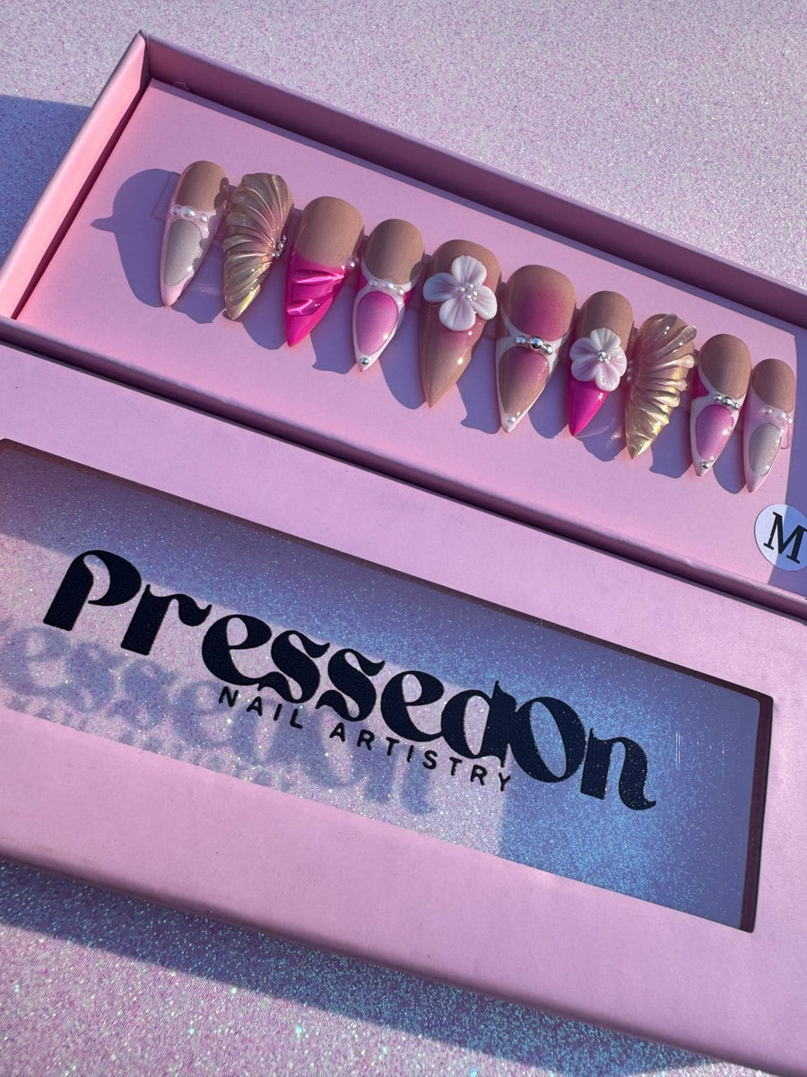 These are pink and neutral-toned mermaid press-on nails with gold accents and 3D flower designs. Some nails also feature pearls and rhinestones.