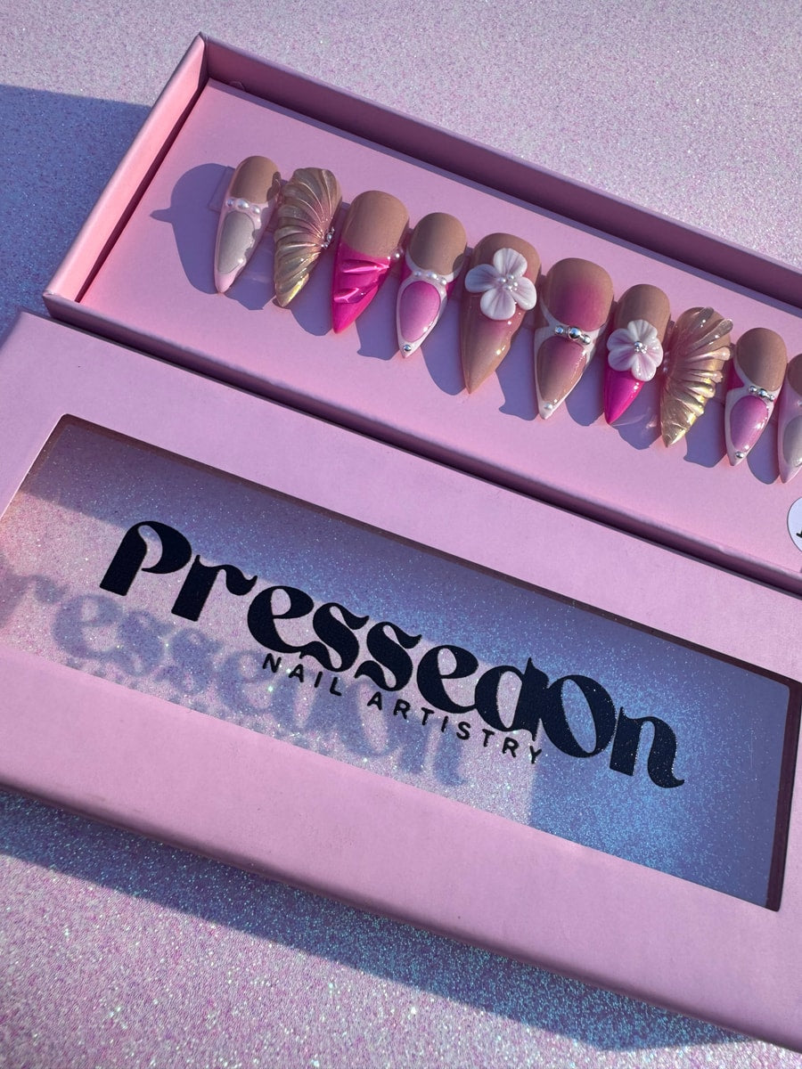 Assortment of pink mermaid press-on nails. The nails feature iridescent accents, flower details, and a medium length.