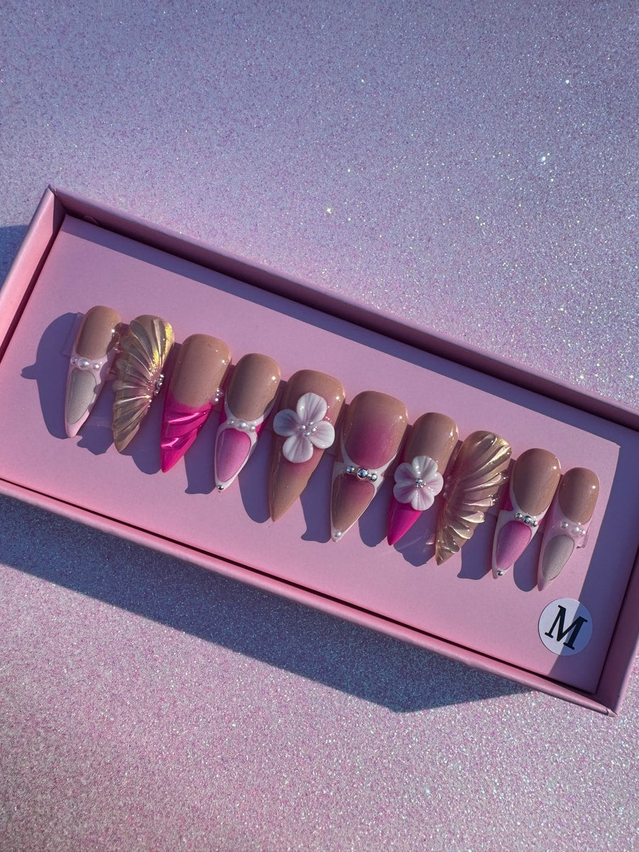 Medium-length press-on nails in a pink and nude color scheme with gold mermaid accents, pearl details, and flower embellishments.