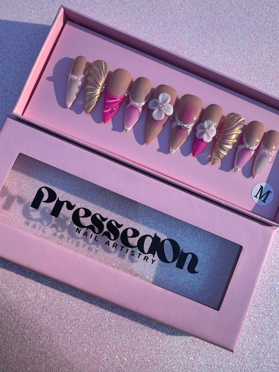 Medium-length press-on nails in pink and nude shades with pearl, flower and metallic embellishments offer a mermaid-inspired look.