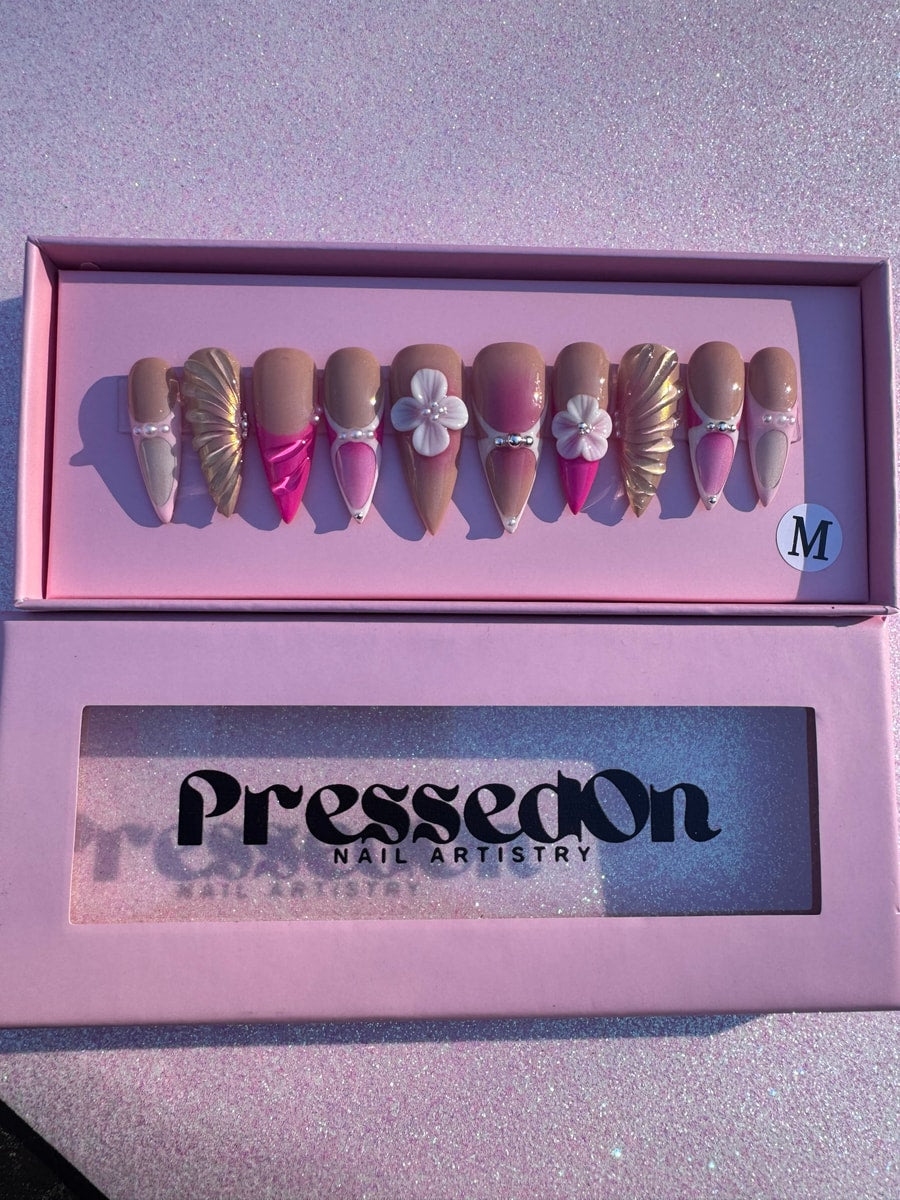 Medium length press-on nails in a pink and nude mermaid design, featuring gold sculpted accents, pearl details, rhinestone embellishments, and 3D flower charms.