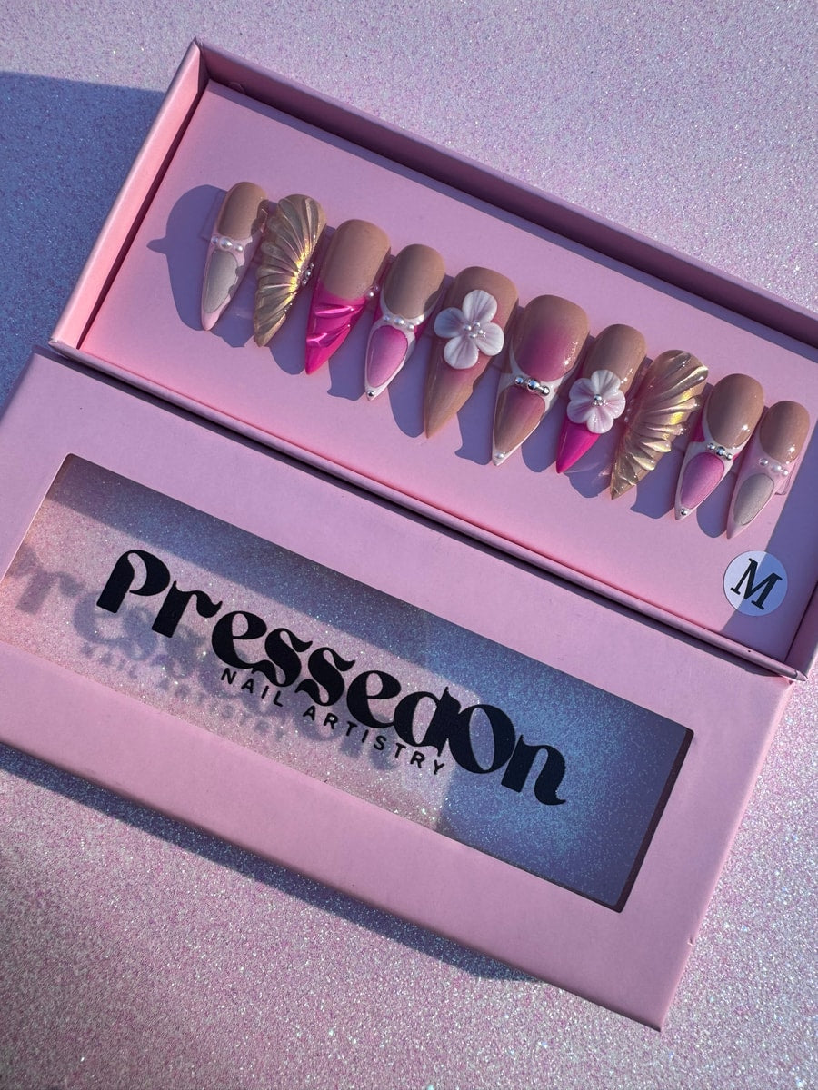 A set of medium-length pink and nude press-on nails with gold mermaid scale accents, pearl embellishments, and 3D flower charms.