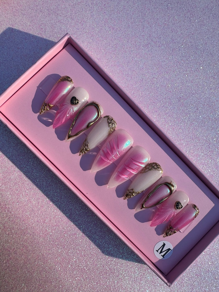 Pink paradise medium press-on nails with stiletto shape and gold accents. Designs include iridescent pink and solid white with embellishments.