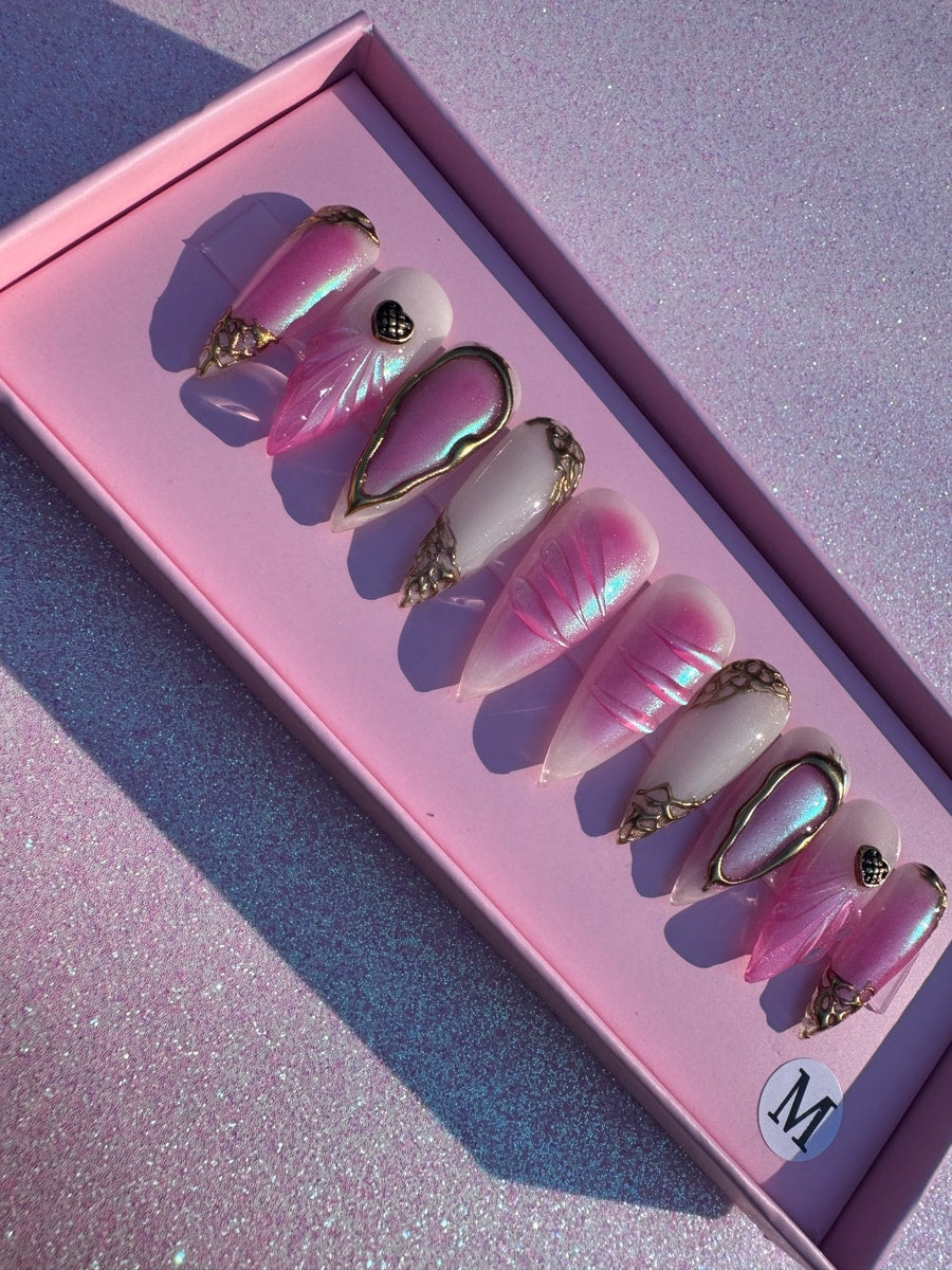 Medium-length pink press-on nails with iridescent shimmer, pearl white accents, gold embellishments, and unique seashell-inspired designs.