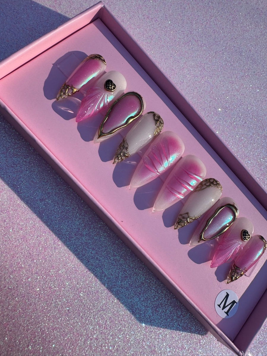 A set of pink paradise press-on nails with gold accents. Some nails are a solid pink shimmer, while others are white with pink details and gold embellishments.