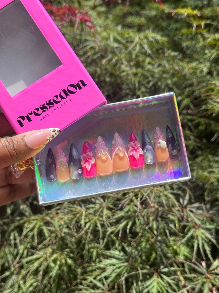 Set of stiletto press-on nails featuring pink, peach, and black colors with 3D flower and shell charms.