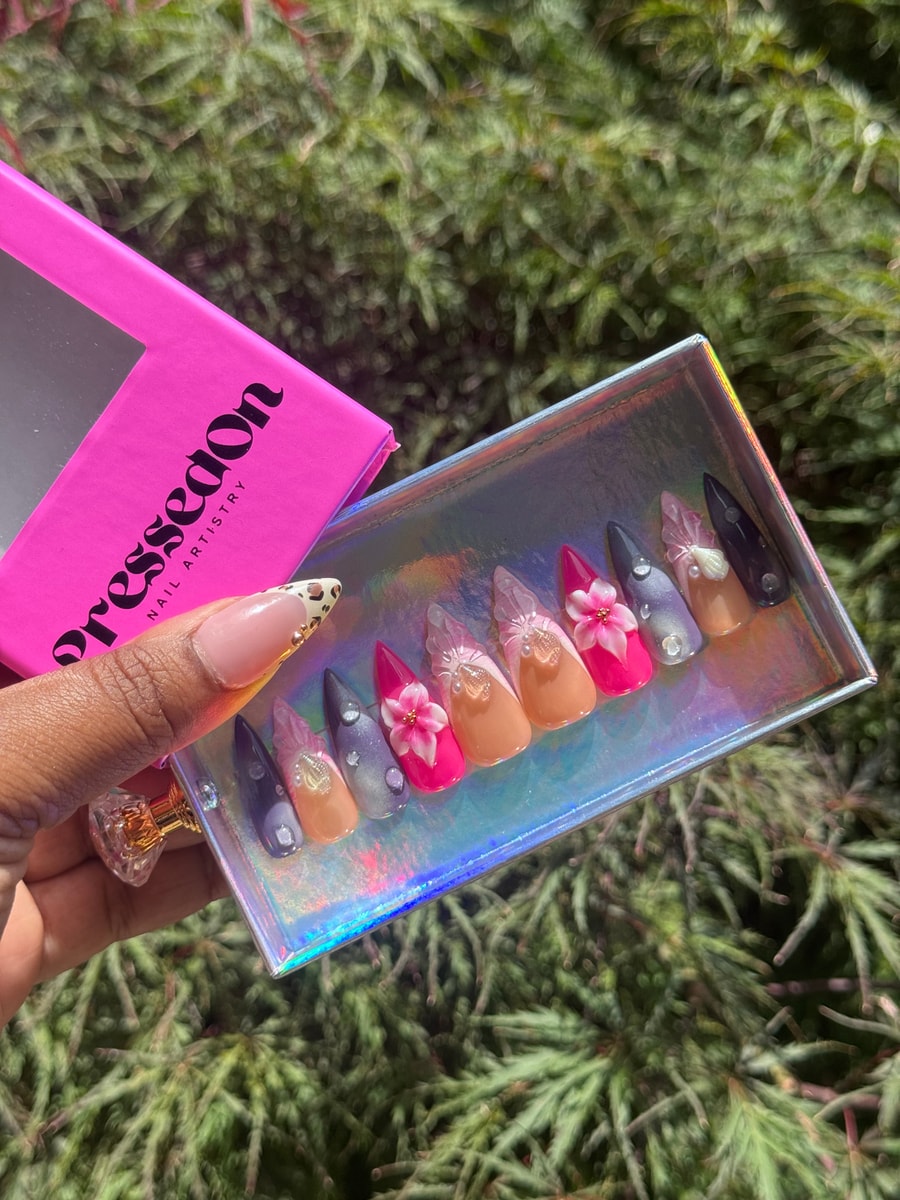 Set of pink press-on nails in varying shades with 3D flower embellishments, pearls, and gems. Nails are medium length and pointed.