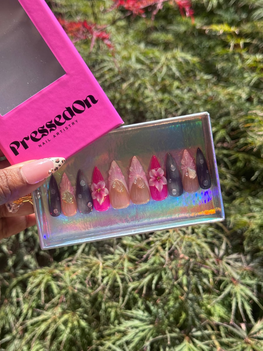 Medium-length press-on nails with a pink pop design, showcasing 3D flower accents and gem embellishments on a variety of nail colors, including pink, nude, and dark purple.