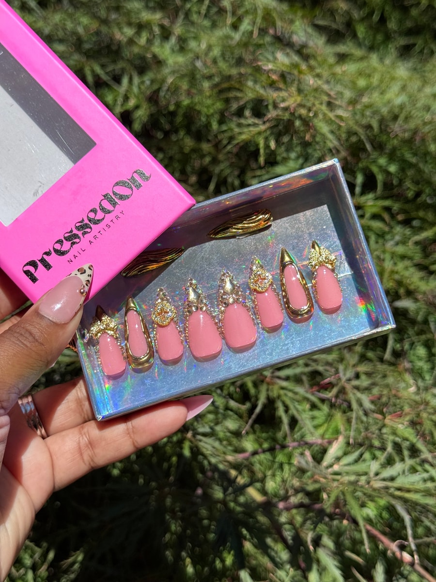 Set of medium-length pink press-on nails with gold trim and rhinestone embellishments.