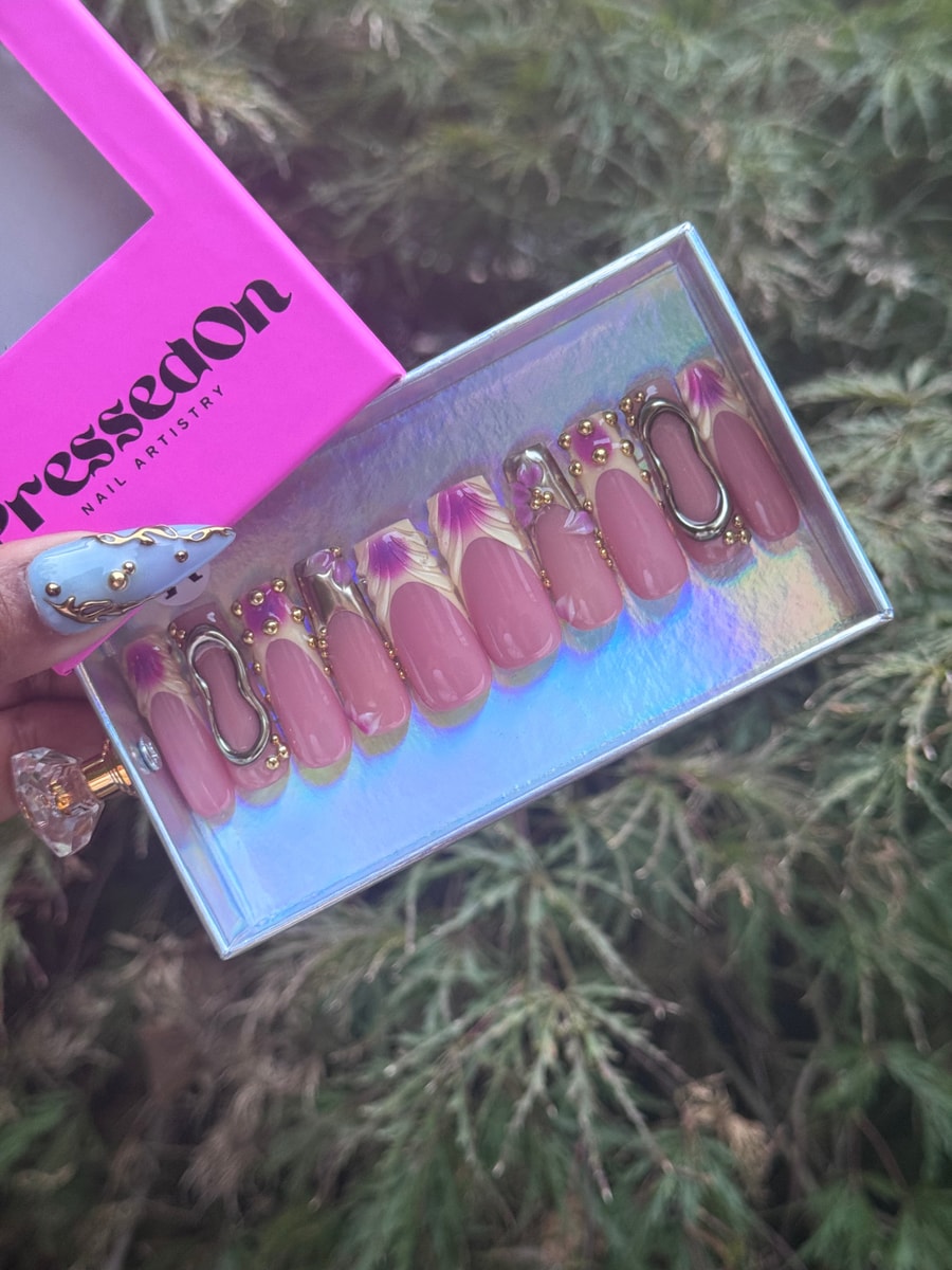 These short pink press-on nails have a unique French floral design in white and purple, with gold beads and silver accents adding a touch of elegance.