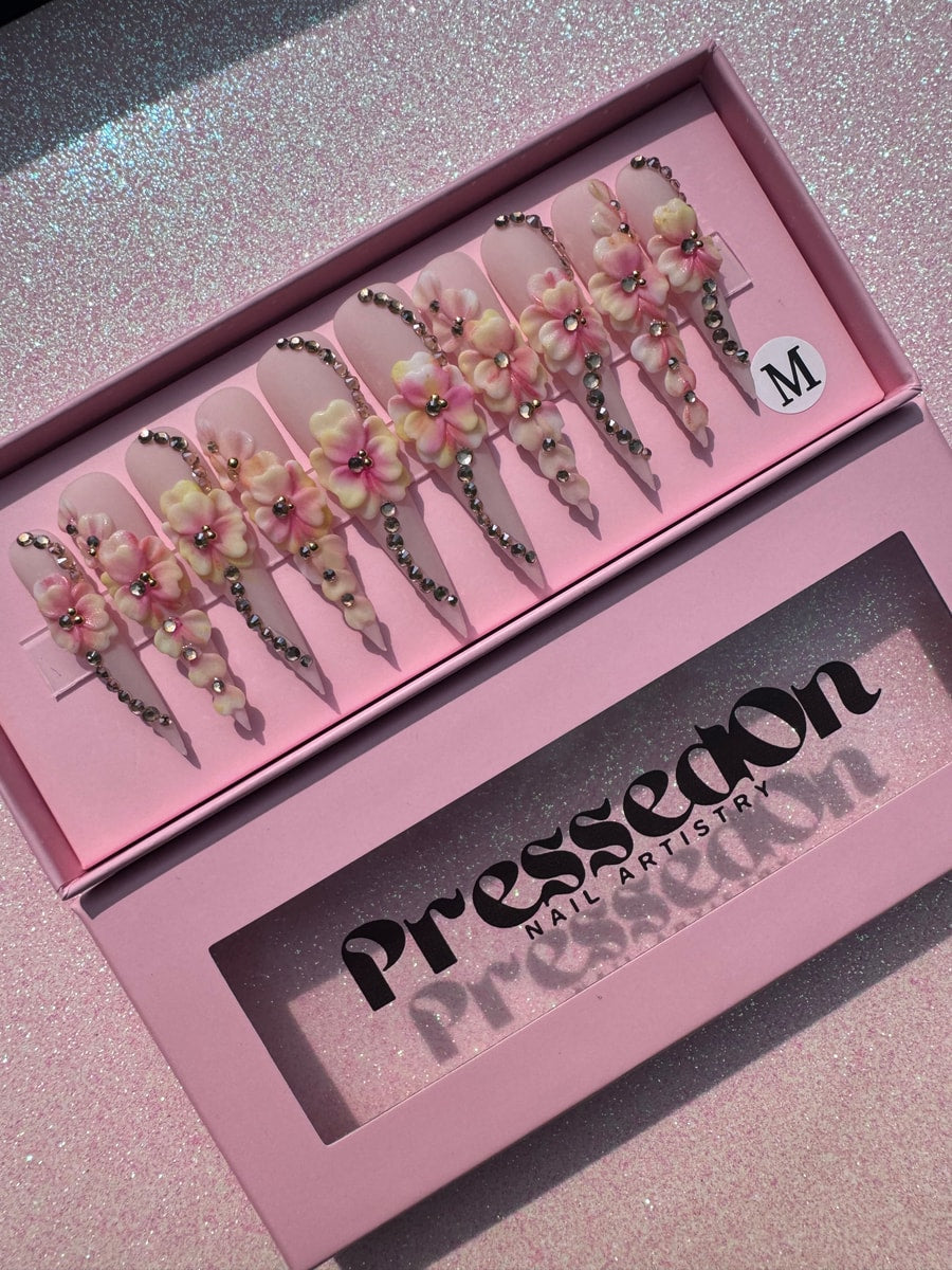 Light pink xtra long stiletto press-on nails are decorated with 3D flowers and rhinestone accents cascading down the nail.