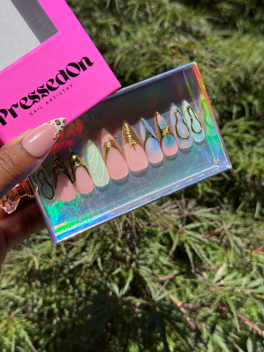 Medium princess-style press-on nails featuring chrome and gold accents in a color palette of pink, white, and blue. Some nails have gold wire designs, others have star charms.