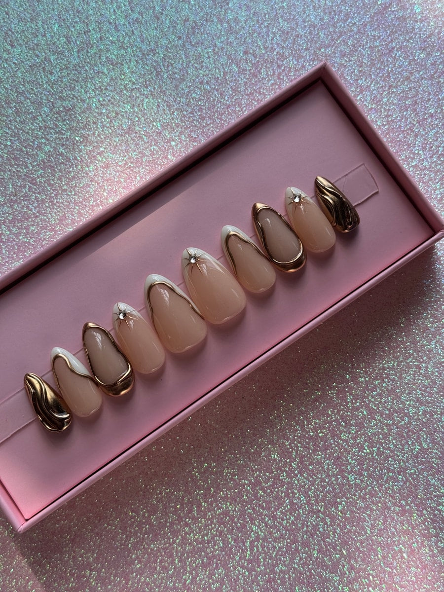 Princess super short press-on nails with a nude base, gold outlines, white tips, and rhinestone accents. Several nails have a unique gold, textured design.