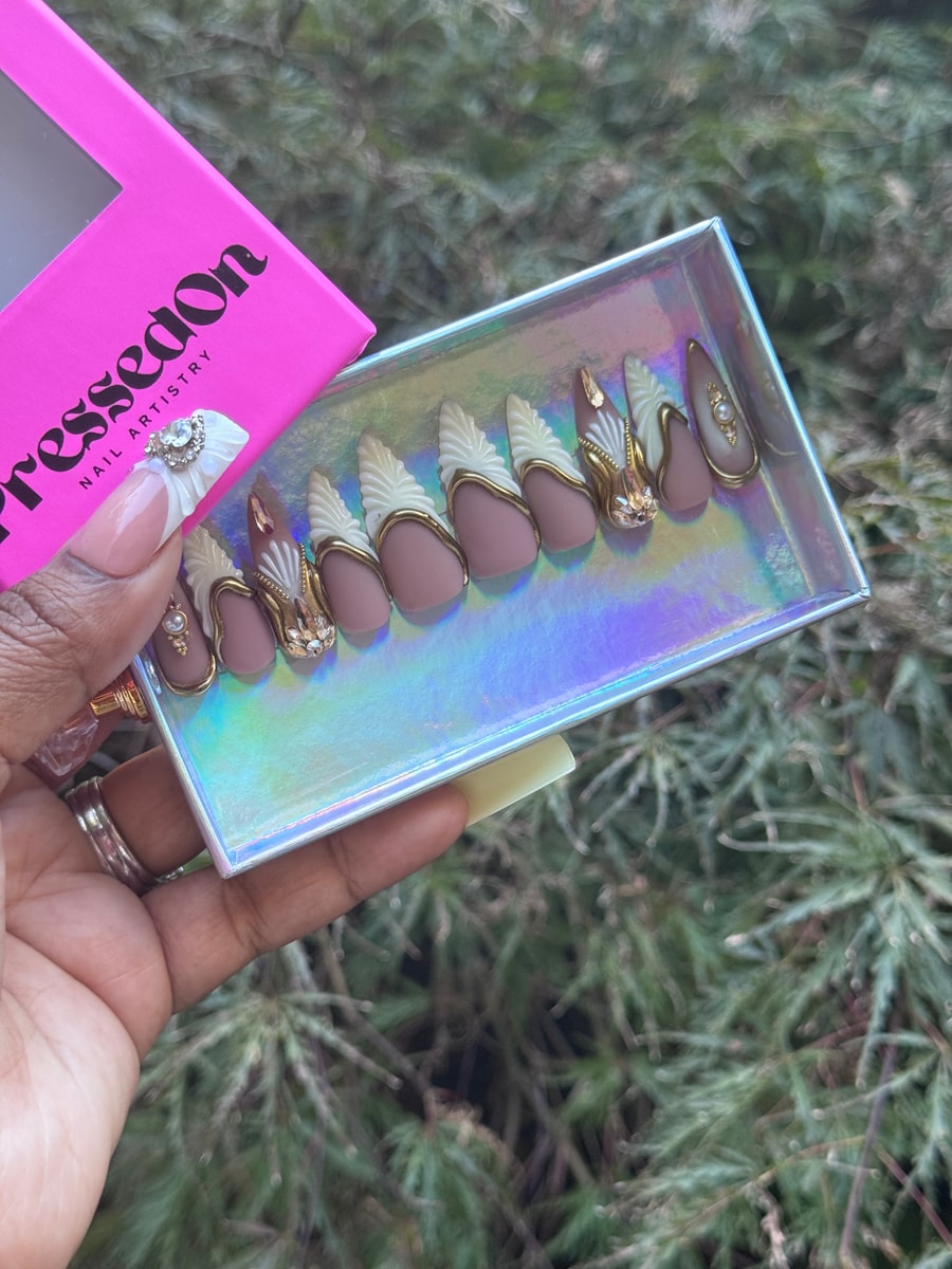 Medium mauve press-on nails feature sculpted white designs with gold trim, along with pearl and rhinestone accents for an elegant, queenly look.